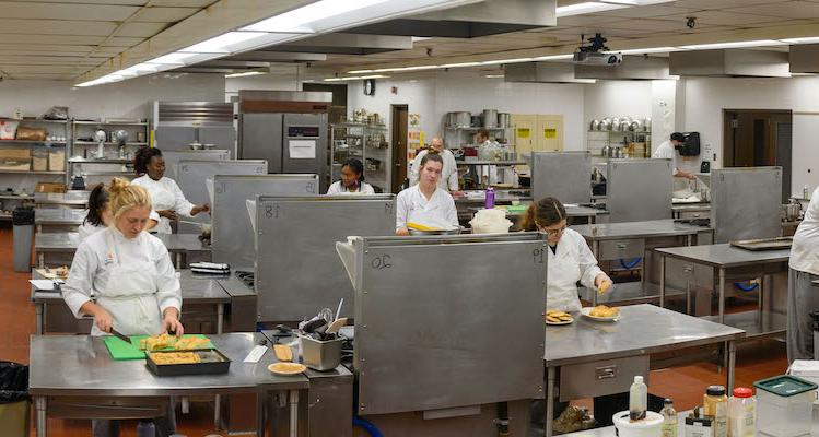 commercial kitchen with culinary arts students preparing food dishes